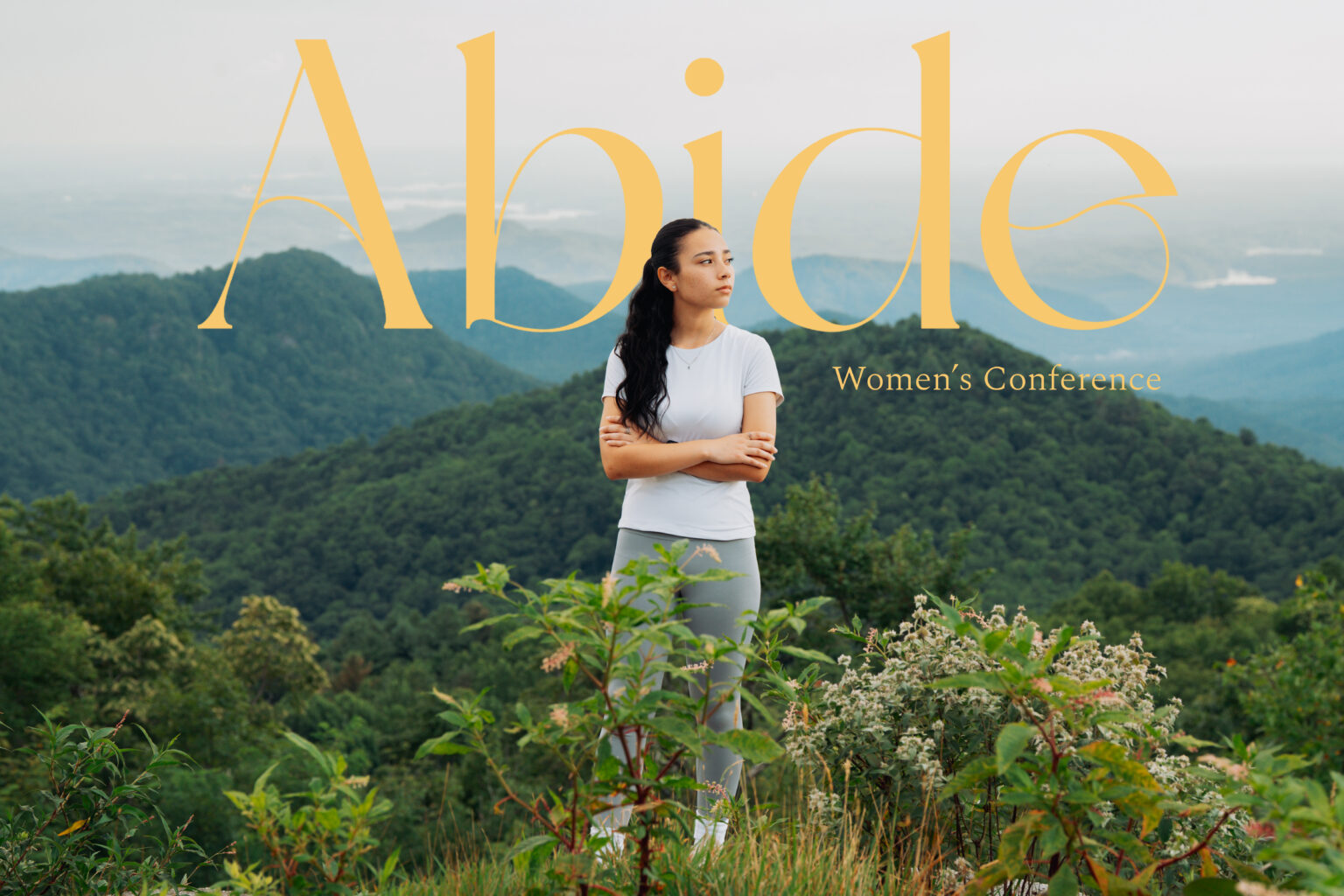 Abide Women's Conference. A woman stands on a mountain overlook beneath the gold Abide title.